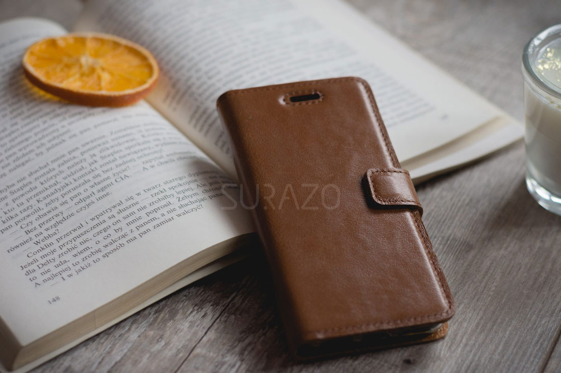 hnědé kožené pouzdro na smartphone ležící vedle knihy na dřevěném stole